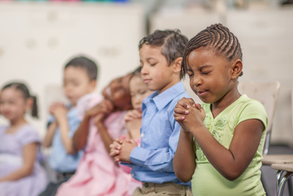 Children praying together in a classroom setting.