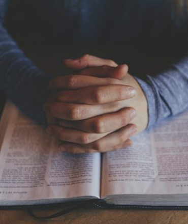 Hands clasped on an open book.