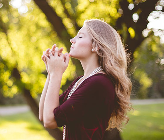 Woman praying outdoors with closed eyes.
