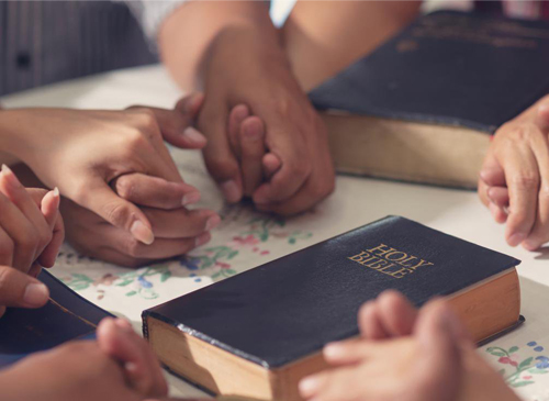 Hands holding a prayer with a Bible.