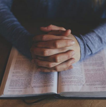 Hands clasped on an open book.
