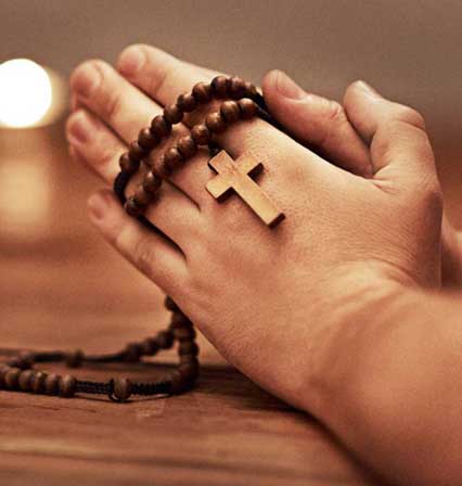 Hands holding a wooden cross necklace.