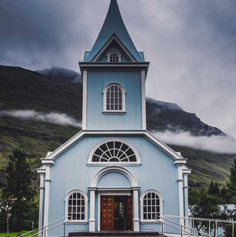 Blue church building against cloudy mountains.