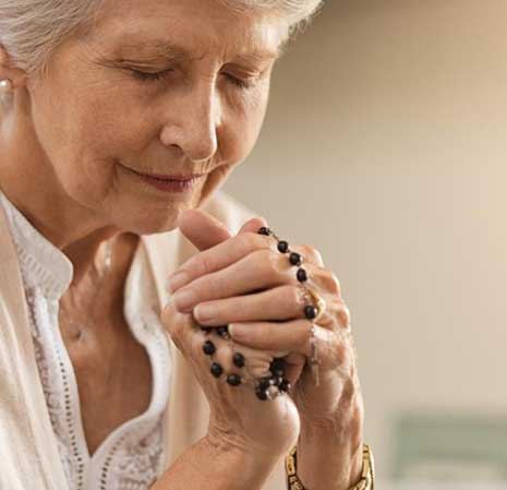 Elderly woman praying with rosary beads.