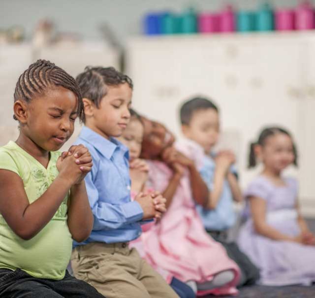 Children praying together in a classroom setting.