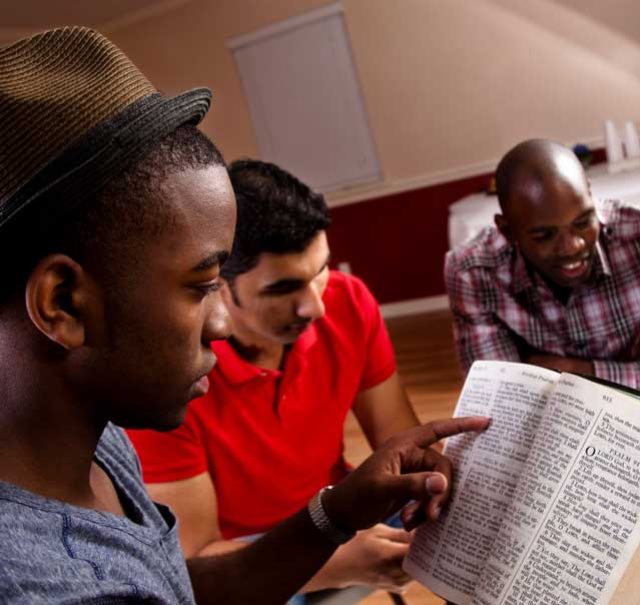 Three men engaged in reading together.